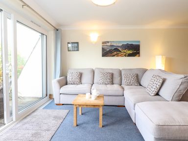 A living room with a gray sectional sofa and wooden coffee table next to sliding glass doors at Pavey Ark in Ambleside