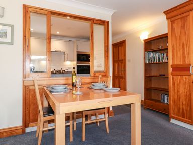 A dining area with a wooden table set for four and a bookshelf in a room at Pavey Ark in Ambleside