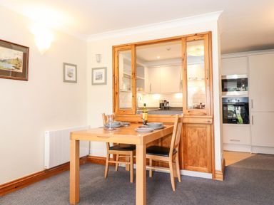A dining area with a wooden table set for two and chairs next to a pass-through window to a kitchen at Pavey Ark in Ambleside