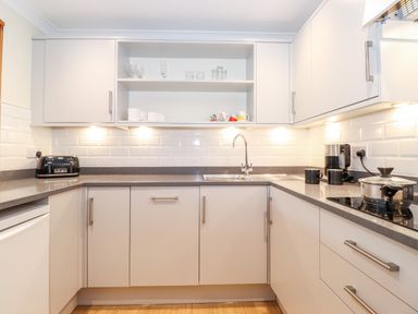 A kitchen with white cabinets gray countertop a sink a toaster a coffee maker cups and a pot on the stove at Pavey Ark in Ambleside