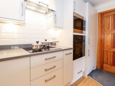 A kitchen with white cabinets two pots on a stove a microwave and oven next to a wooden door at Pavey Ark in Ambleside