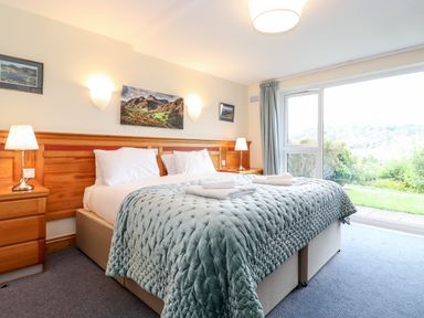 A bedroom with a double bed two bedside tables and lamps a large window shows a garden at Pavey Ark in Ambleside