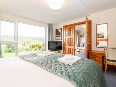 A bedroom with a bed and towels on it a television a wooden desk and chair and a view of a sitting room through wooden doors at Pavey Ark in Ambleside