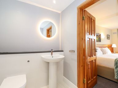 A bathroom with a sink and round mirror next to a doorway leading to a bedroom at Pavey Ark in Ambleside