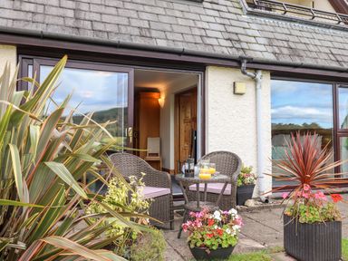 An outdoor patio with two wicker chairs a small round table with drinks plants and flowers at Pavey Ark in Ambleside