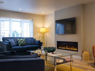 A living room with blue sofas a glass coffee table a corner floor lamp a wall-mounted television and a modern fireplace at The Neon Rose in Bowness-On-Windermere