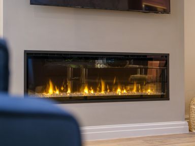 A built-in rectangular electric fireplace with flames and decorative glass stones at The Neon Rose in Bowness-On-Windermere
