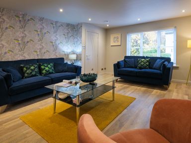A living room with two blue sofas a glass coffee table a yellow rug and an orange chair at The Neon Rose in Bowness-On-Windermere