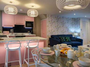 A kitchen with pink cabinets and marble countertops next to a living room with a blue sofa and floral wallpaper at The Neon Rose in Bowness-On-Windermere