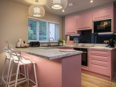 A kitchen with pink cabinets white bar stools and marble countertops at The Neon Rose in Bowness-On-Windermere