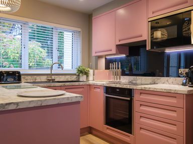 A kitchen with pink cabinets marble countertops a sink a window with blinds and a built in oven at The Neon Rose in Bowness-On-Windermere