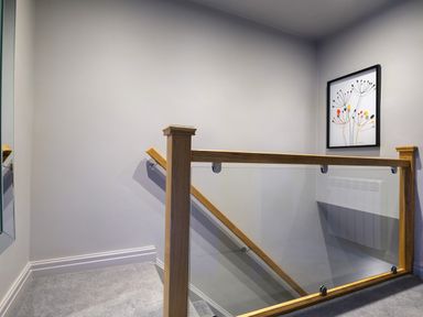 A staircase with wooden and glass railing and a framed artwork on the wall at The Neon Rose in Bowness-On-Windermere