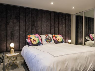 A bedroom with a large bed with pillows featuring colorful artwork and bedside tables with lamps at The Neon Rose in Bowness-On-Windermere