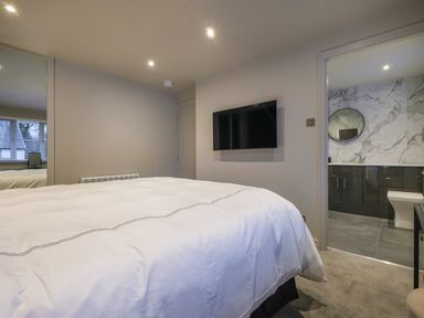 A bedroom with a bed a wall-mounted TV and an adjoining bathroom with a sink and toilet at The Neon Rose in Bowness-On-Windermere