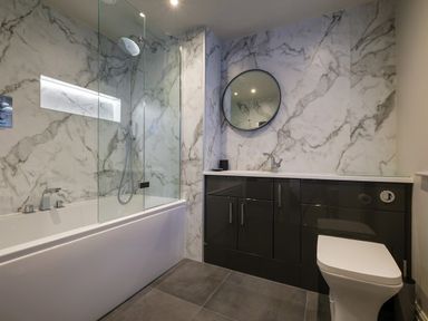 A bathroom with a bathtub shower combination black cabinets round mirror and a toilet at The Neon Rose in Bowness-On-Windermere