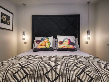 A bedroom with a bed with angel printed pillows and a patterned blanket at The Neon Rose in Bowness-On-Windermere