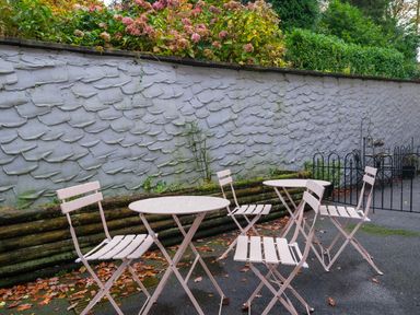 An outdoor patio area with metal tables and chairs near a textured wall and plants
