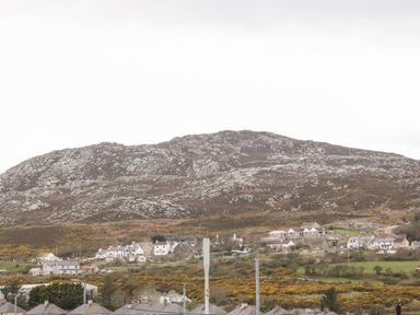 A hillside with scattered houses and bushes below a rocky hill at Glasfryn in Holyhead
