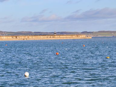 A body of water with several buoys and a long stone pier in the background at Glasfryn in Holyhead