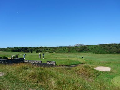 A golf course with people playing golf and green hills in the background at Glasfryn in Holyhead