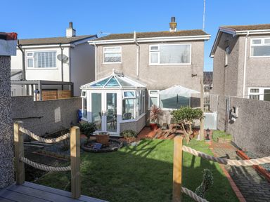 A backyard garden with green grass a glass conservatory wooden picnic table with umbrella and potted plants at Glasfryn in Holyhead