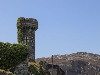 A stone castle tower with ivy covering part of it and mountains in the background at Glasfryn in Holyhead
