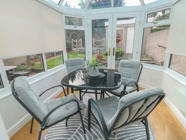 A conservatory with a glass table and four chairs at Glasfryn in Holyhead