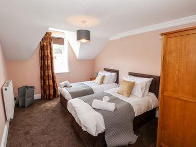 A bedroom with two single beds with gray throws and pillows a wooden wardrobe and a window with curtains at Oakhurst in Keswick