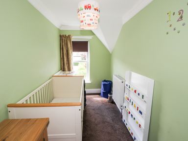 A small nursery with a white crib a wooden dresser a window with a brown blind and curtain green walls with alphabet magnets on a white board and a blue laundry hamper in the corner at Oakhurst in Keswick