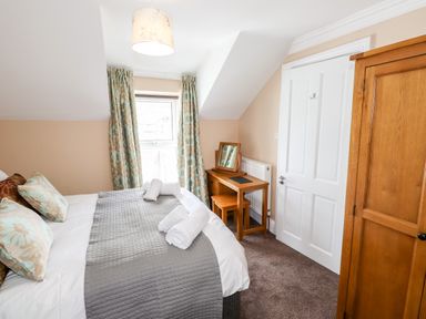 A bedroom with a bed, rolled towels, a wooden wardrobe, a desk with a mirror and a chair at Oakhurst in Keswick