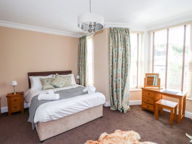 A bedroom with a bed pillows and bedside tables next to windows with curtains and a dressing table with a stool at Oakhurst in Keswick