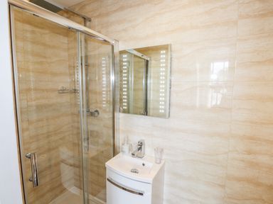 A bathroom with a glass shower enclosure a white sink cabinet and a mirror with lights at Oakhurst in Keswick