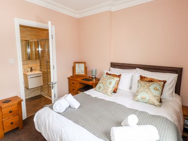 A bedroom with a double bed, two bedside tables, a dressing table, and an open door to an ensuite bathroom at Oakhurst in Keswick