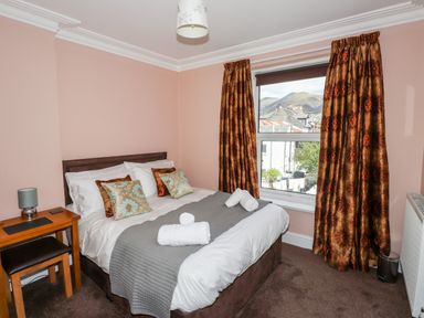 A bedroom with a double bed with pillows and rolled towels beside a window with curtains at Oakhurst in Keswick