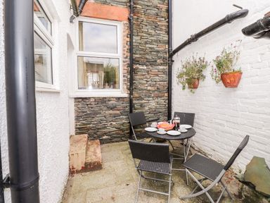 An outdoor patio with a round table set for tea and four chairs with a stone wall and hanging flower pots at Oakhurst in Keswick