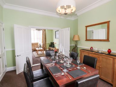 A dining room with a wooden table set with glasses and cutlery and leather chairs with a cabinet and mirror on the wall at Oakhurst in Keswick