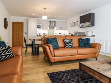 A living room with brown leather sofas blue and black patterned cushions a wooden coffee table and a kitchen area at 2 Pensyflog Barns in Porthmadog