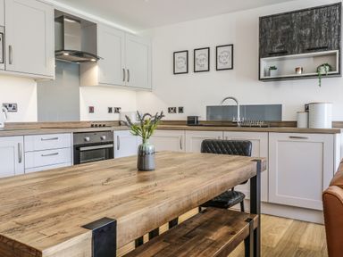 A kitchen with wooden table and chairs white cabinets and framed pictures on the wall at 2 Pensyflog Barns in Porthmadog