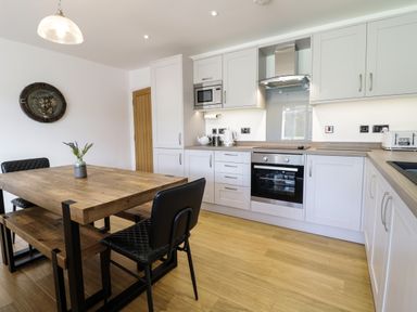 A kitchen with dining table black chairs wooden floor and white cabinets at 2 Pensyflog Barns in Porthmadog
