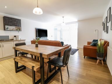 An open plan living room and kitchen with wooden dining table and bench two leather sofas and a wall mounted TV at 2 Pensyflog Barns Porthmadog