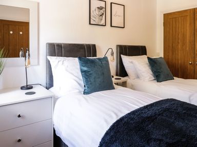A bedroom with two single beds white bedding blue pillows bedside tables and lamps at 2 Pensyflog Barns in Porthmadog