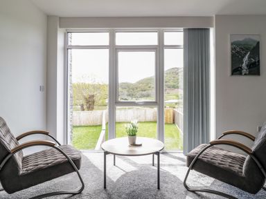 A sitting area with two chairs and a round table in front of large windows overlooking a garden at 2 Pensyflog Barns in Porthmadog