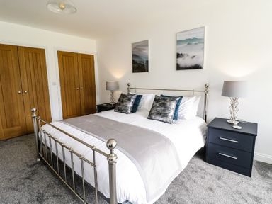 A bedroom with a metal bed frame two bedside tables with lamps and wooden wardrobes at 2 Pensyflog Barns in Porthmadog