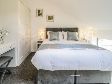 A bedroom with a double bed bedside tables and lamps a wardrobe and a dressing table with a stool at 2 Pensyflog Barns in Porthmadog