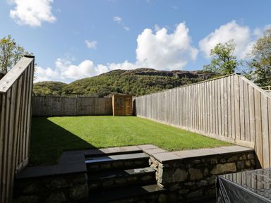 A fenced backyard with a small shed at the far end and a stone step entrance at 2 Pensyflog Barns in Porthmadog