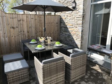 An outdoor patio with a dining table and chairs under an umbrella with a wooden fence and stone wall at 2 Pensyflog Barns in Porthmadog