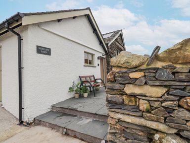 An entrance with steps leading to a door a bench and potted plants beside a stone wall at Old Howgate Barn Outgate near Hawkshead