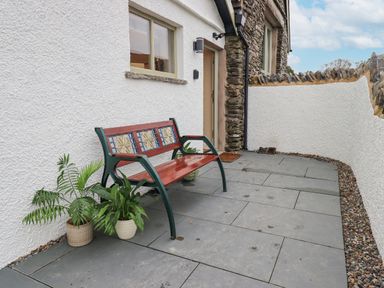 An outdoor patio with a wooden bench and potted plants near a white wall at Old Howgate Barn Outgate near Hawkshead