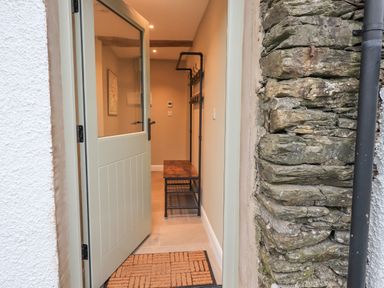 An open front door showing an entryway with a wooden bench and coat rack at Old Howgate Barn Outgate near Hawkshead