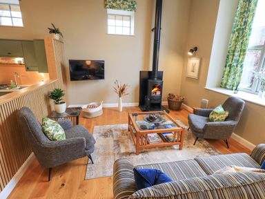 A living room with two armchairs a wood stove and a coffee table at Old Howgate Barn Outgate near Hawkshead